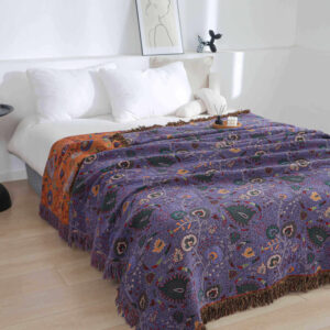Reversible jacquard throw blanket in purple and orange tones laid on bed