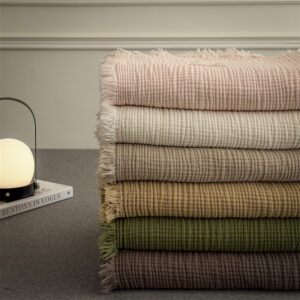 Stacked fringed cotton gauze blankets in neutral and earth tones – breathable, fringed boho home textiles.
